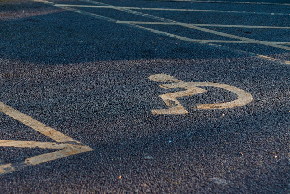 Close-up view of a numbered parking space on an asphalt surface, with the number '22' painted in white visible in the foreground. The parking area features parallel white lines marking individual bays, with some diagonal lines nearby. The asphalt appears slightly textured, and the environment suggests an outdoor parking lot adjacent to a residential or commercial property. This image illustrates the importance of understanding parking and access regulations during house removals and furniture transport, a key consideration for Man and Van Wallington when planning efficient home relocation and packing and moving services, especially around SM6 areas.